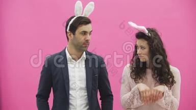年轻漂亮的夫妇站在粉红色的背景上。 在这期间，他们穿着杂乱的耳朵。 温柔地看着